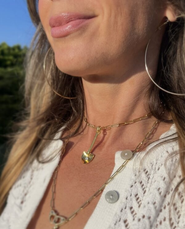 Layered gold charm necklaces on a woman in sunlight, styled with a white crochet blouse.